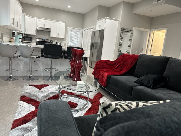 Una sala de estar moderna con un sofá gris, una manta roja y una mesa de centro de vidrio.