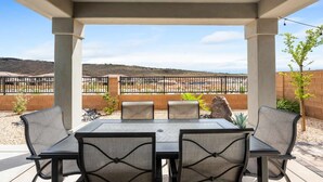 An outdoor patio with a table and chairs, a view of a desert landscape, and a brick wall. - Pool View at Paseos by RedAwning (Washington)