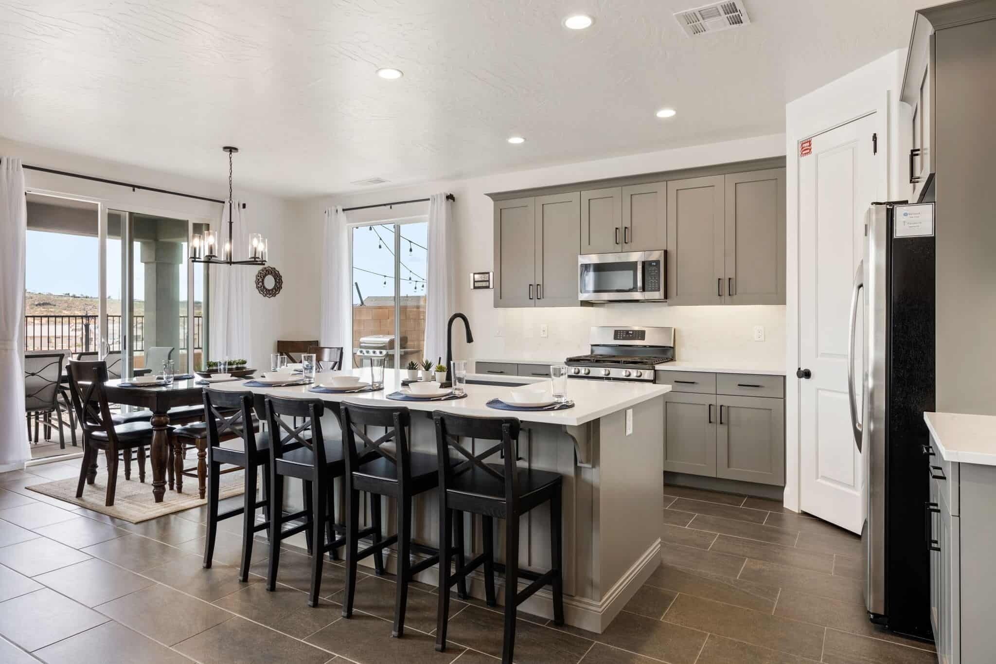 A modern kitchen with a central island, stainless steel appliances, and a dining area with dark chairs.