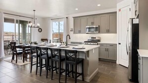 A modern kitchen with a central island, stainless steel appliances, and a dining area with dark chairs. - Pool View at Paseos by RedAwning (Washington)