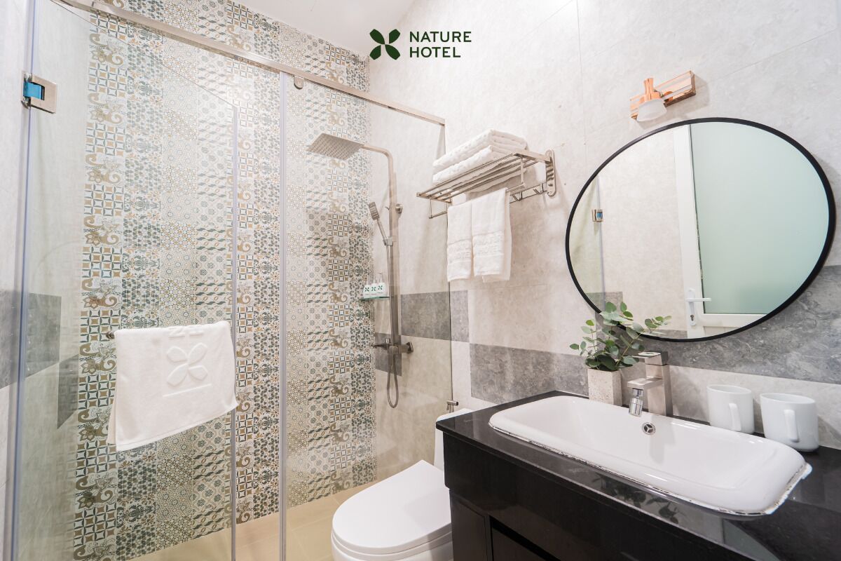 A modern bathroom with a glass-enclosed shower, a white toilet, a black sink, and a round mirror.
