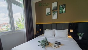 Une chambre d’hôtel avec un grand lit, une vue sur la ville par la fenêtre et un mur décoré sur le thème de la nature.