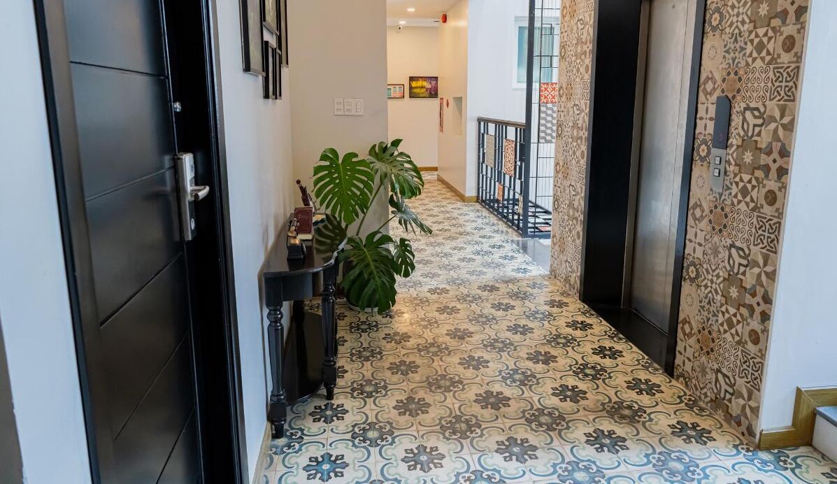 A hallway with patterned floor tiles, a potted plant, and a door on the left.