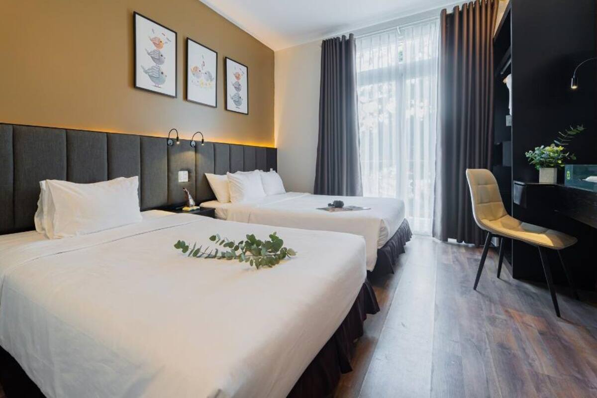 A hotel room with two beds, a desk, and a chair. There are three framed pictures on the wall.