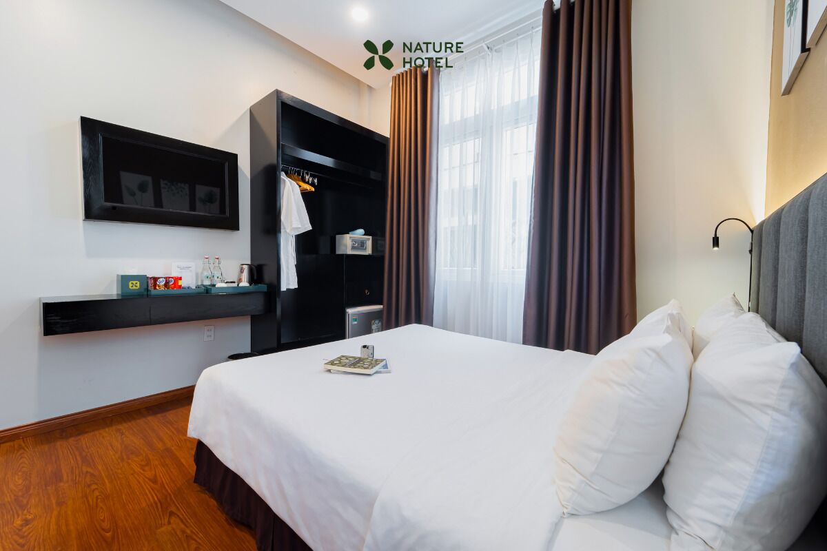 Quarto de hotel com cama, televisão na parede, armário e janela com cortinas.