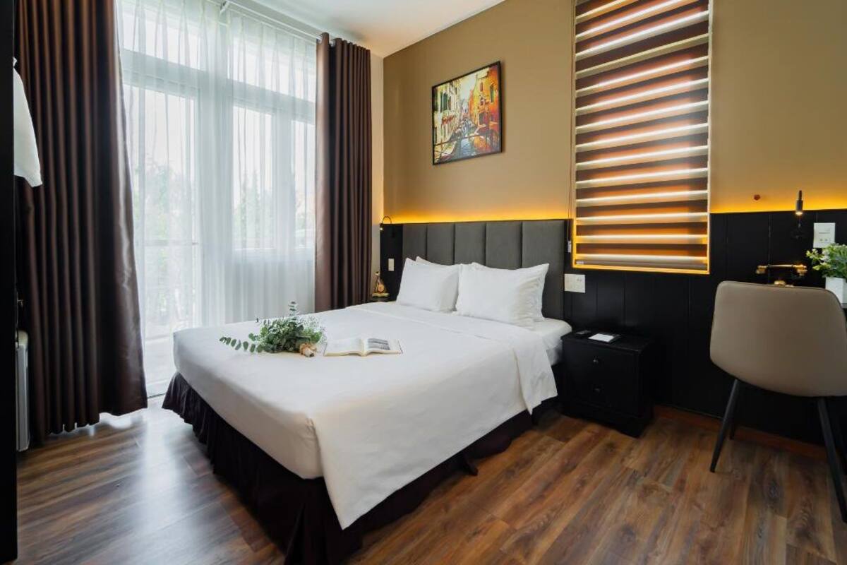 A hotel room with a large bed, a bedside table, a chair, and a painting on the wall.