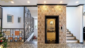 Un hall d’hôtel avec un escalier, un mur décoratif orné de motifs géométriques, et un panneau indiquant l’emplacement des chambres et du hall d’accueil.