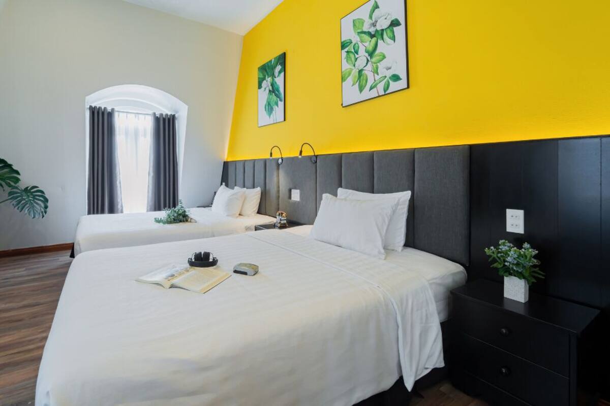 A hotel room with two beds, a desk, a chair, and a large window with curtains.