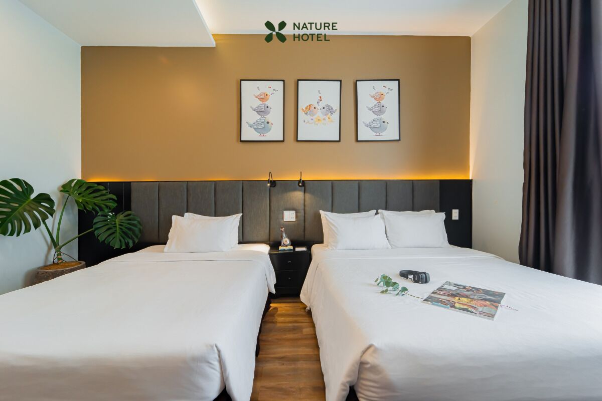 A hotel room with two beds, a headboard, wall art, a nightstand, and a potted plant.