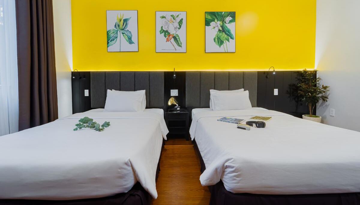 A hotel room with two beds, a nightstand, a lamp, and wall art.