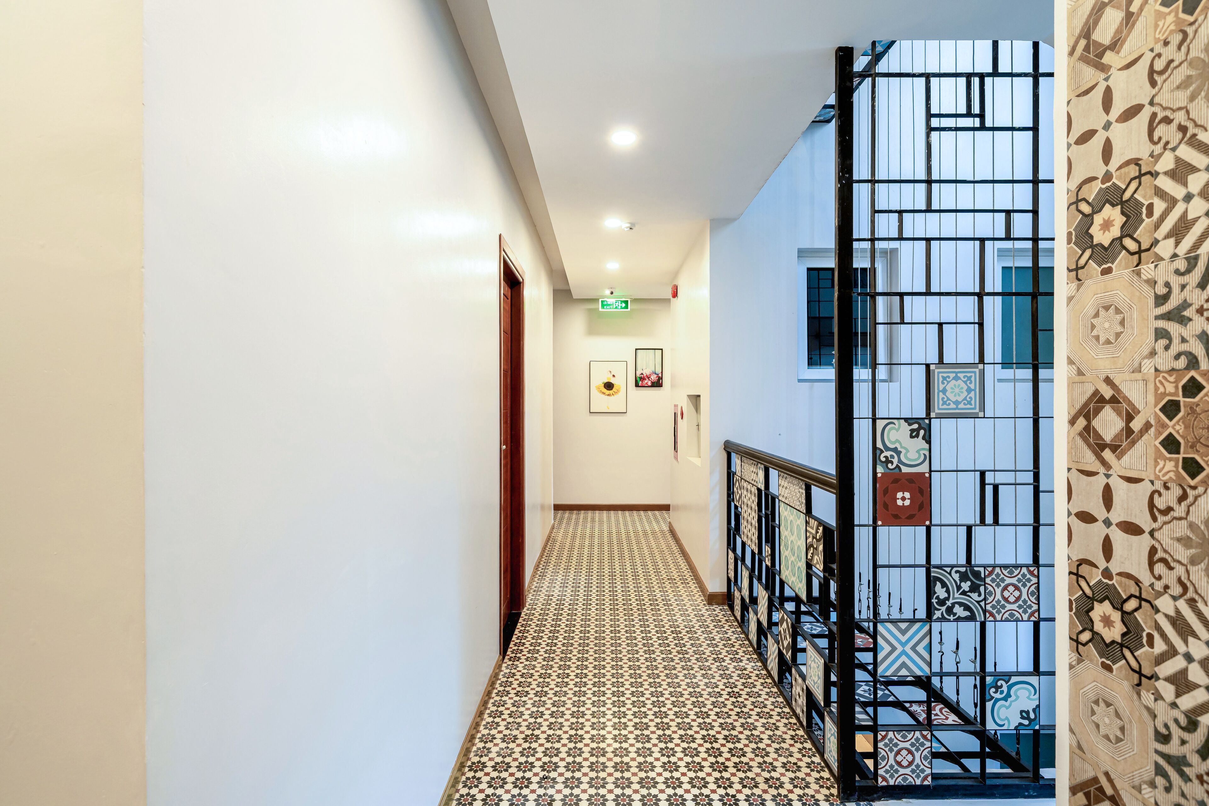 A hallway with patterned floor tiles, a staircase with a black railing, and a wall with decorative tiles.