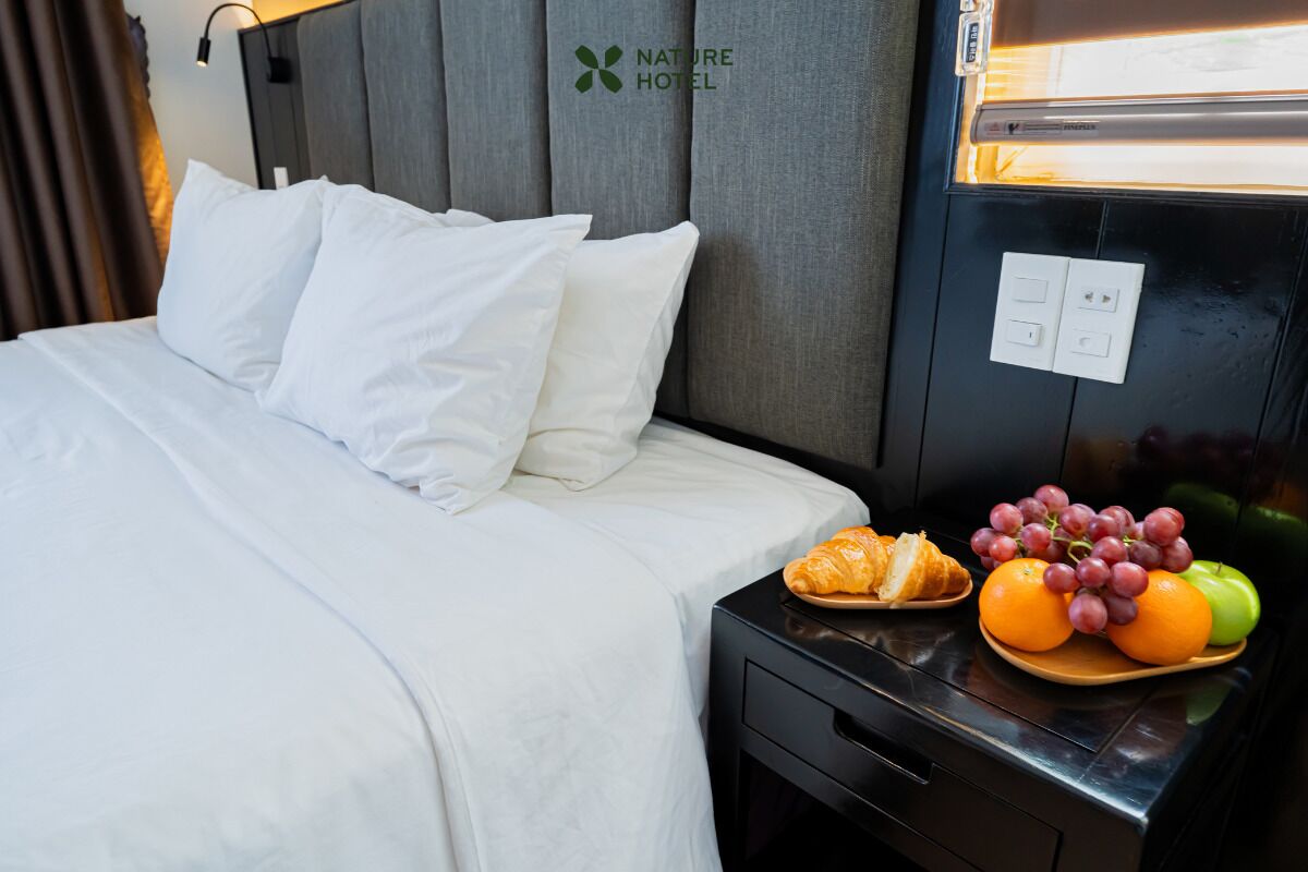 Een hotelkamer met een bed, een nachtkastje met een schaal fruit en een hoofdbord met het hotel logo.