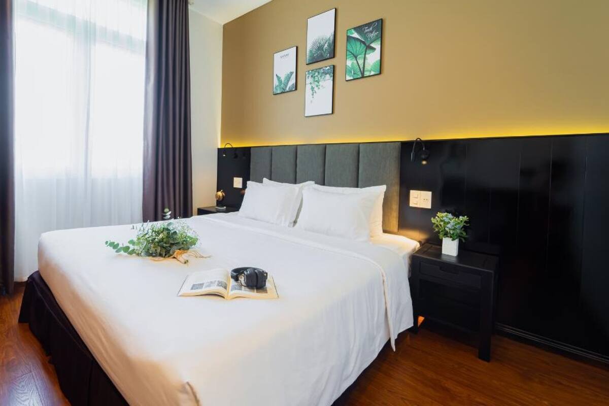 A hotel room with a large bed, a nightstand, a wall-mounted lamp, and framed artwork.