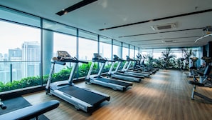 Une salle de sport équipée de tapis de course, de poids et de grandes fenêtres donnant sur la ville.