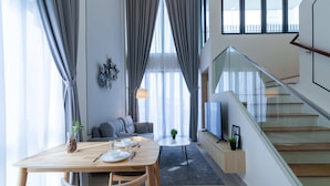 Un salon moderne comprenant un coin repas, un escalier et une grande fenêtre agrémentée de rideaux.