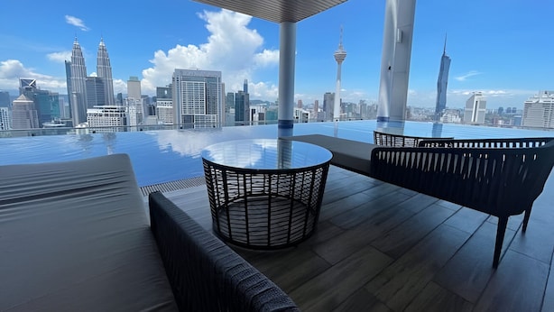 Une terrasse sur le toit avec une table en verre, des chaises en osier noir et une vue sur les toits de la ville.