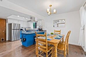 Eine moderne Küche mit einer zentralen Kochinsel, Edelstahlgeräten und einem Essbereich mit Holztischen und -stühlen.
