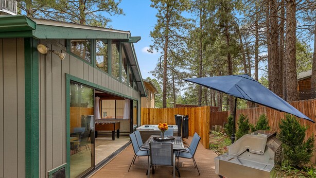 A patio with a table and chairs, a grill, and a wooden fence.