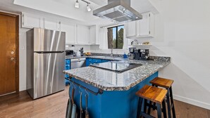 A modern kitchen with a stainless steel refrigerator, a granite countertop island with stools, and white cabinetry.