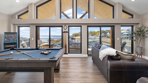 A spacious living area with a pool table, a sofa, and a view of the outdoors through large windows. - AMAZING Lakeview, Private Putting Green, Hot Tub, Pools, Pool Table, Pickleball (Branson)