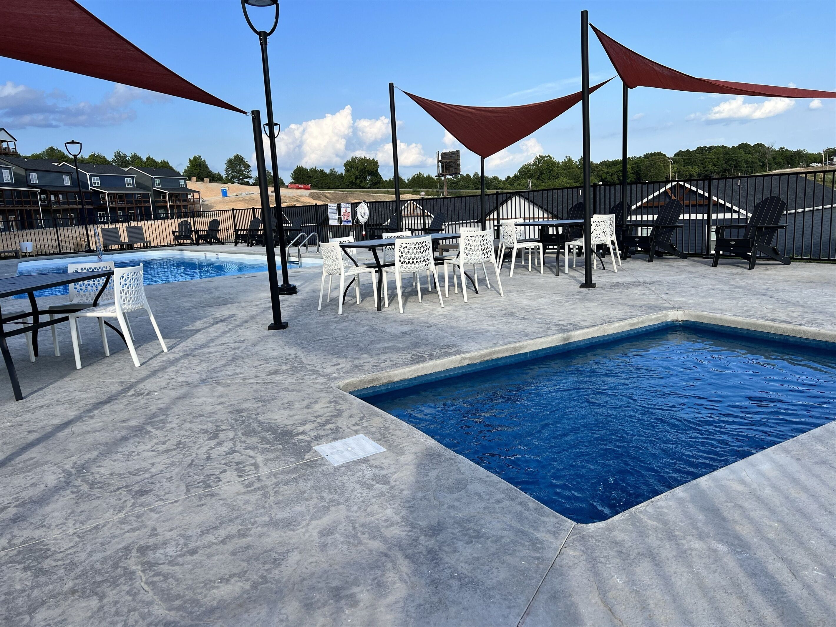 A pool area with a rectangular pool, white chairs, and tables.