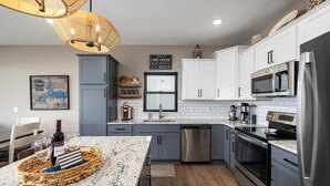 A modern kitchen with granite countertops, stainless steel appliances, and a dining area with a table set for two. - AMAZING Lakeview, Private Putting Green, Hot Tub, Pools, Pool Table, Pickleball (Branson)