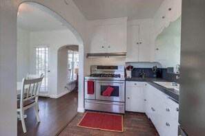 A kitchen with white cabinets, a stainless steel stove, and a red rug. - Welcoming Bungalow with 2nd BR/Office & Chef's Kitchen (La Mesa)