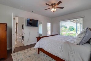 Ein Schlafzimmer mit einem Bett, einem Deckenventilator, einem Fernseher und einem Fenster mit Jalousien.