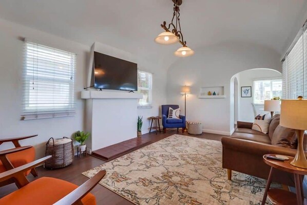 Ein Wohnzimmer mit flachbildfernseher an der Wand, einem blauen Sessel, einem braunen Sofa und einem gemusterten Teppich.