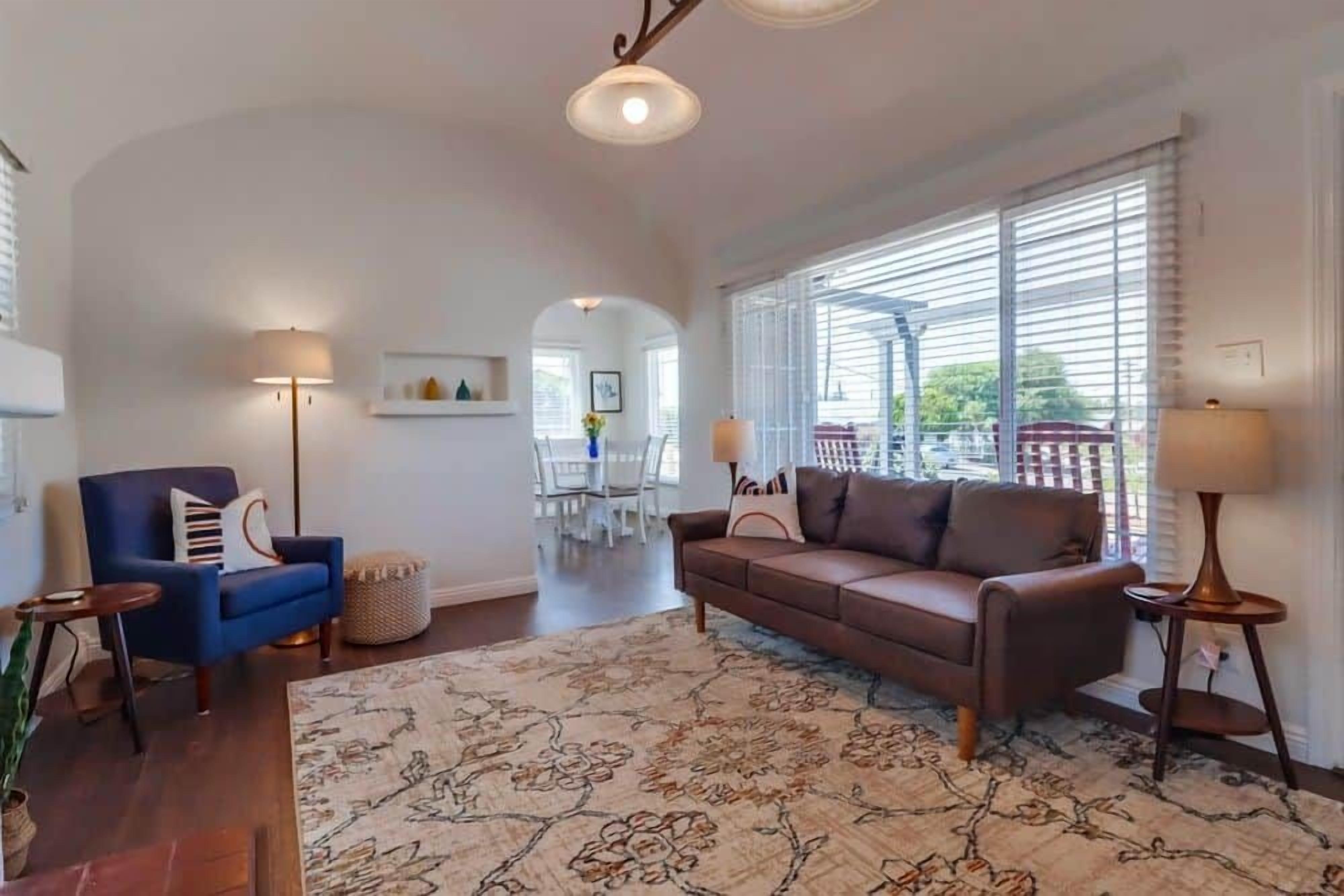 A spacious living room with a brown sofa, blue armchair, and a patterned rug.