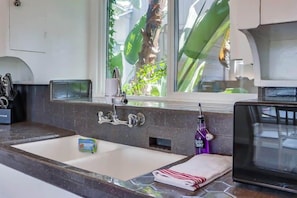 Une salle de bain avec un grand lavabo, un miroir et une fenêtre donnant sur des palmiers.