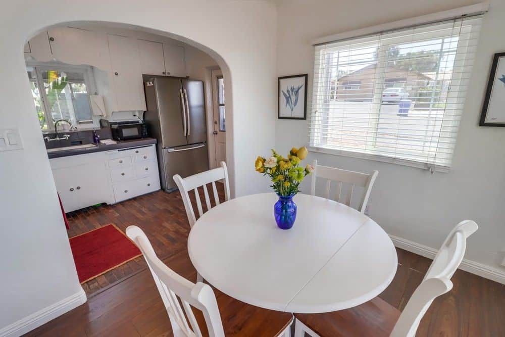 A compact kitchen with modern appliances, a dining table with chairs, and a window with blinds.