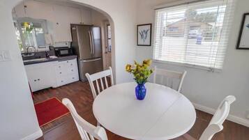A compact kitchen with modern appliances, a dining table with chairs, and a window with blinds.