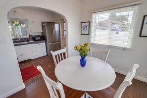 A compact kitchen with modern appliances, a dining table with chairs, and a window with blinds. - Welcoming Bungalow with 2nd BR/Office & Chef's Kitchen (La Mesa)