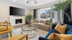 Un salon moderne comprenant un canapé, des fauteuils, une table basse en verre, une cheminée et un grand téléviseur.