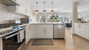 Une cuisine moderne avec des armoires blanches, des appareils en acier inoxydable et des luminaires suspendus.