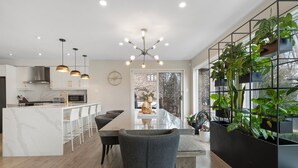 Une cuisine moderne dotée d’un îlot central, de luminaires suspendus et d’un pot de fleurs noir contenant des plantes.