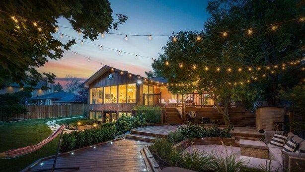 Une maison moderne dotée d’une terrasse, d’un espace salon extérieur et de guirlandes lumineuses.