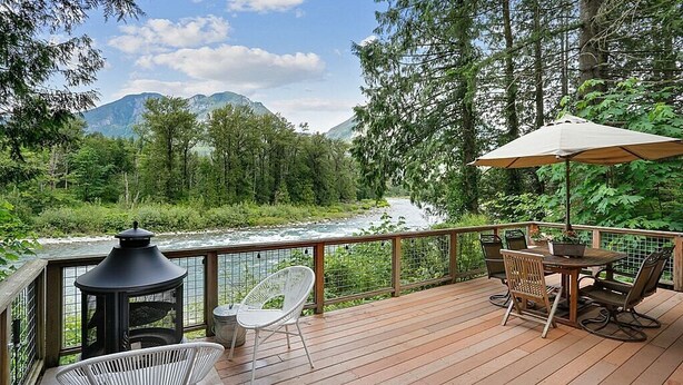 A wooden deck with outdoor furniture, a lantern, and a view of a river and mountains.