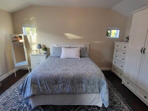 A bedroom with a bed, a dresser, a nightstand, a lamp, and a window.