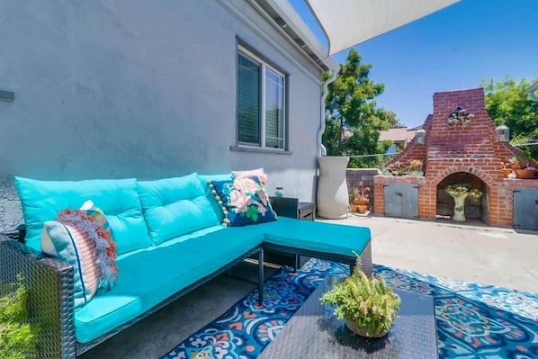 A turquoise sofa with a patterned rug, a brick barbecue, and a potted plant.