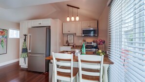 A modern kitchen with white cabinetry, a stainless steel refrigerator, a microwave, and a dining area with a wooden table and white chairs.