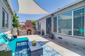 Une terrasse avec des meubles d’extérieur, une cheminée en briques et une grande fenêtre avec des stores.