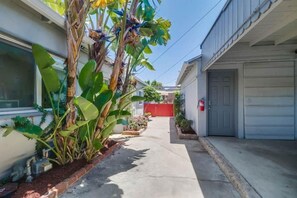 A residential driveway with a garage door, a red gate, and a variety of plants.