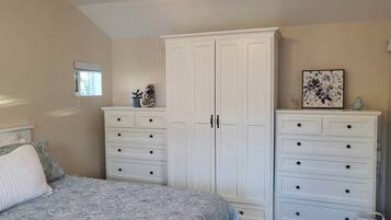 A bedroom with a bed, two white dressers, a window, and a ceiling light.
