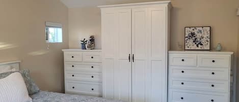 A bedroom with a bed, two white dressers, a window, and a ceiling light.