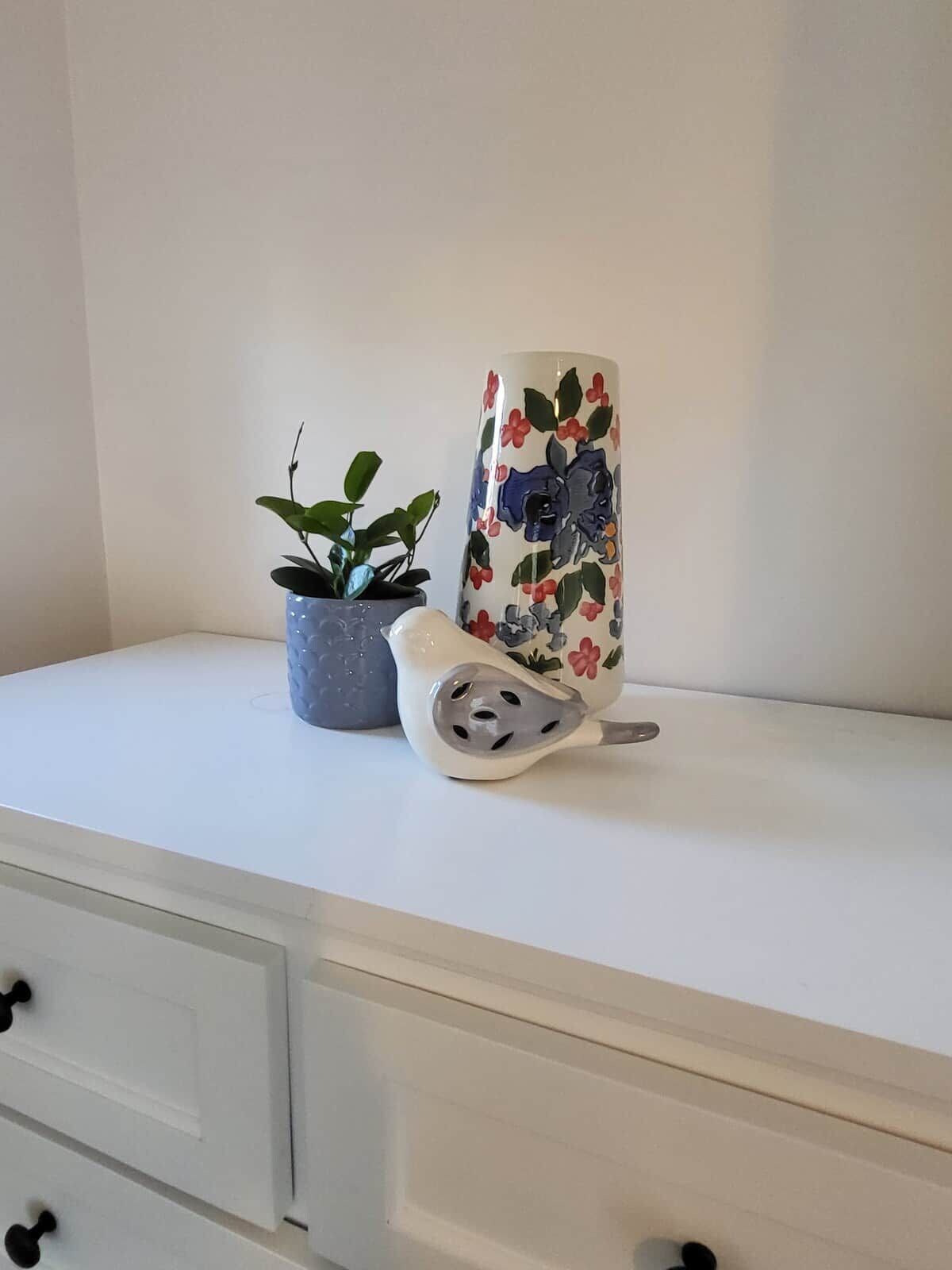 A white dresser with a potted plant and a ceramic vase with a floral pattern.