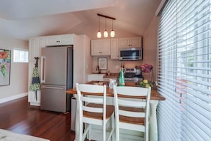 A kitchen with white cabinets, a stainless steel refrigerator, a microwave, and a dining area with two white chairs.