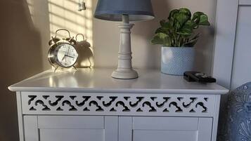 A white bedside table with a blue lamp, a clock, and a plant.