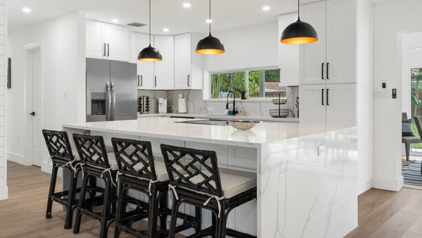A modern kitchen with white cabinetry, a large island with bar stools, and pendant lighting. - Delila's Chic 3 Bedroom-2 bath w/ Heated Pool + Game Room (Deerfield Beach)